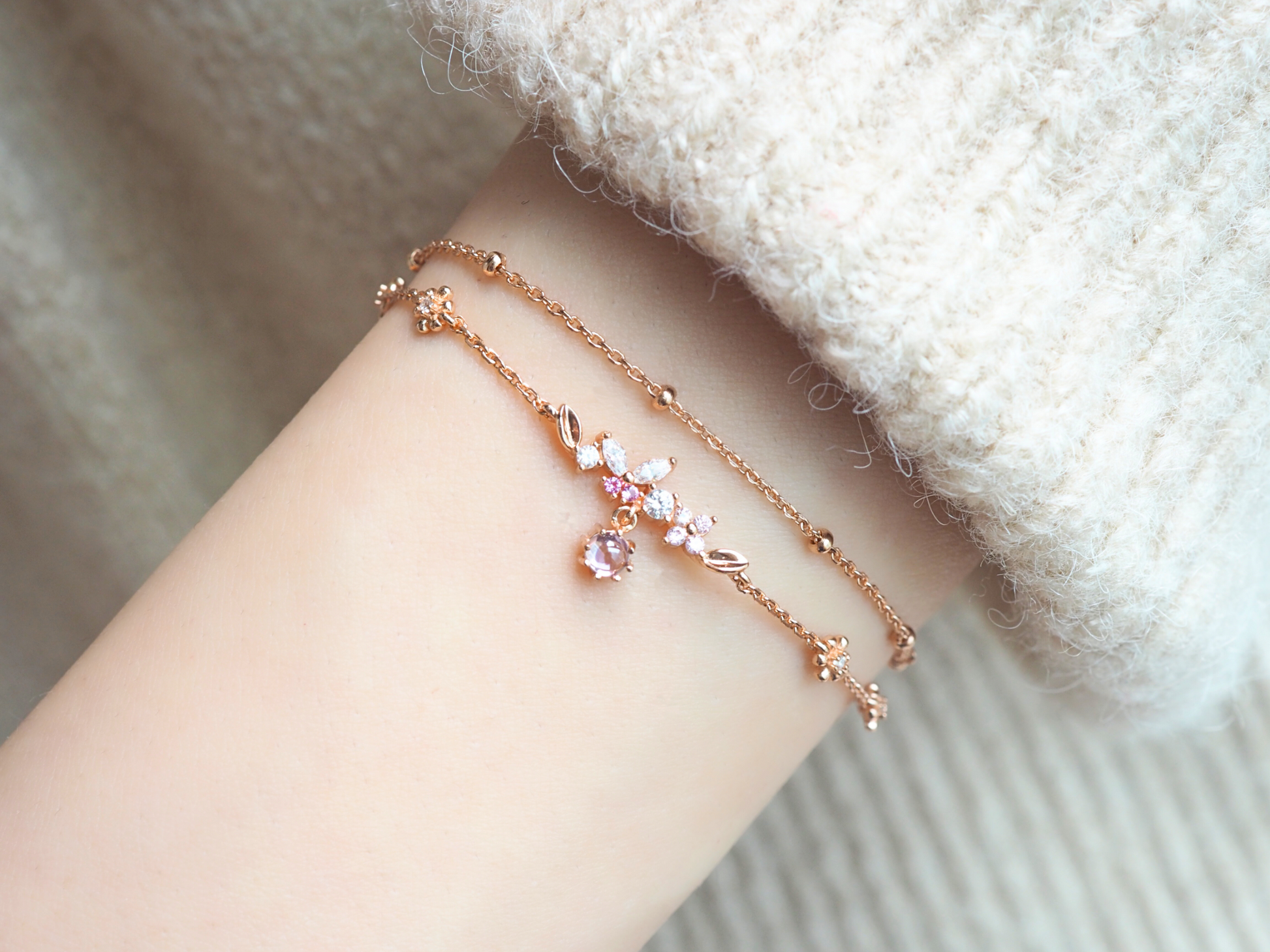 This image shows a person's arm wearing a beautiful rose gold bracelet. The chain is set with a row of tiny butterfly-shaped zircons and delicate floral decorations. A pink gemstone is set in the center.