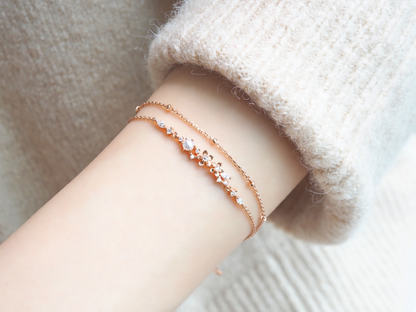 This image shows a person's arm wearing a delicate rose gold colored double bracelet. The bracelet is made up of rows of tiny zircons and beautifully decorated with flowers and pearls.