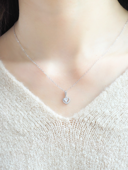 This picture shows the upper body of a woman wearing a beautiful silver necklace. The necklace has a heart-shaped pendant with a sparkling zirconium in the center.