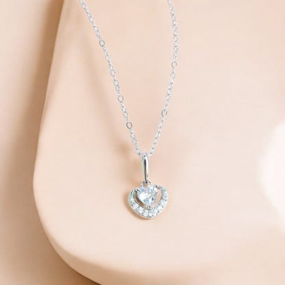 This picture shows a silver heart pendant necklace. The pendant has a sparkling heart shaped zircon in the center surrounded by a circle of crushed stones.